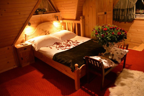 Knusse chalet slaapkamer met rozenblaadjes op bed en bloemen, warme houten sfeer in Tsjechië.