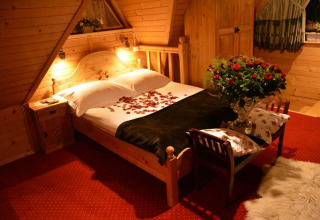 Knusse chalet slaapkamer met rozenblaadjes op bed en bloemen, warme houten sfeer in Tsjechië.