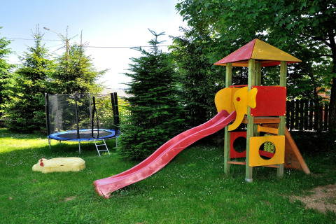 Speeltuin met glijbaan, trampoline en zandbak in een tuin bij een chalet in de Tsjechische bergen.