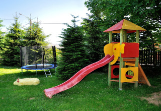 Speeltuin met glijbaan, trampoline en zandbak in een tuin bij een chalet in de Tsjechische bergen.