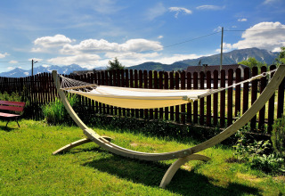 Een hangmat in een zonnige tuin met houten omheining en bergzicht bij een chalet in Tsjechië.
