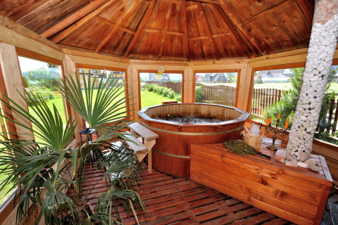 Overdekte houten zithoek met warmwaterbad, planten en grote ramen bij een chalet in Tsjechië.