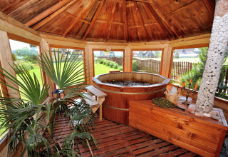 Overdekte houten zithoek met warmwaterbad, planten en grote ramen bij een chalet in Tsjechië.