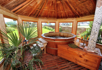 Overdekte houten zithoek met warmwaterbad, planten en grote ramen bij een chalet in Tsjechië.