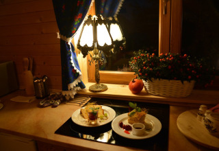 Knusse chaletkeuken met eten op borden, een tafellamp, bloemenmand en verlicht raam 's avonds.