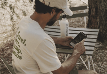 Mann mit Kappe sitzt draußen am Tisch, sieht auf sein Handy im Bell Tent bei Wecamp Jávea, Spanien.