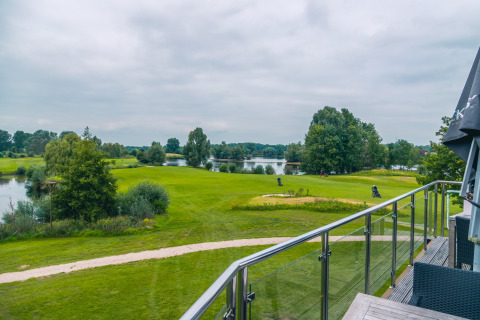 Uitzicht vanaf een glamping-accommodatie op een golfbaan met meren, paden en groene bomen.