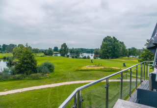Uitzicht vanaf een glamping-accommodatie op een golfbaan met meren, paden en groene bomen.