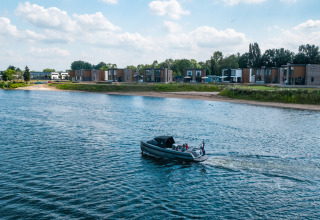 Hébergements glamping modernes en bord de l’eau, avec cabanes et bateau naviguant sur la rivière calme.