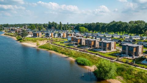 Vista aerea di moderne strutture glamping sul lago, immerse nel verde e nella natura incontaminata.