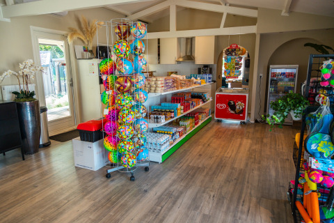 Boutique de glamping avec ballons colorés, snacks, boissons et congélateur à glaces, ambiance lumineuse.