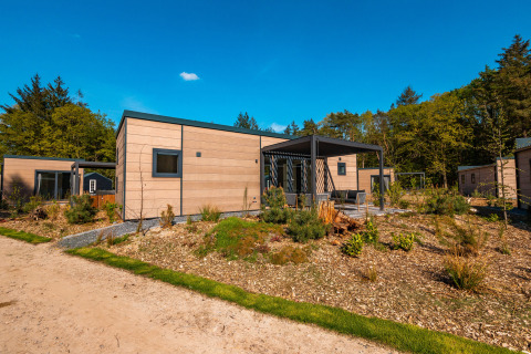 Modern Groeneborg lodge with hot tub, surrounded by greenery, trees, and a clear blue sky above.