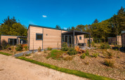 Moderne Groeneborg Lodge mit Hottub, eingebettet in grüne Natur und Bäume bei sonnigem Wetter.