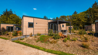 Moderne Groeneborg lodge met hottub, gelegen tussen groen, bomen en onder een heldere blauwe hemel.
