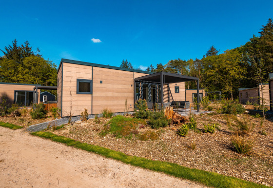 Modern Groeneborg lodge with hot tub, surrounded by greenery, trees, and a clear blue sky above.
