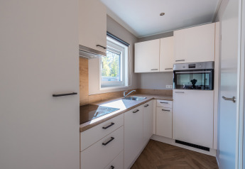 Cucina moderna e compatta con mobili bianchi, forno incassato e finestra che lascia entrare la luce.