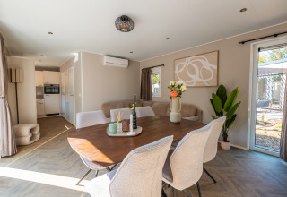 Moderne lodge met eetruimte, lichte stoelen, planten en ramen met zicht op een groene tuinomgeving.