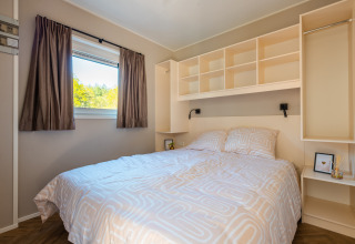 Bright and cozy bedroom with double bed, window, and open storage at Groeneborg Lodge in the Netherlands.