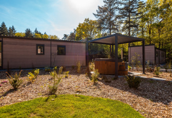 Udsigt til Groeneborg lodge med hottub under pavillon ved Vakantiepark De Wiltzangh, omgivet af skov.