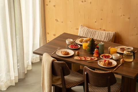 Breakfast setup at a lodge, featuring pastries, orange juice, fruit and candles on a dark wooden table.