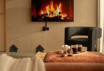 Acogedor interior de lodge con chimenea en la TV, sillón moderno y bandeja con snacks en De Weelderik, Países Bajos.