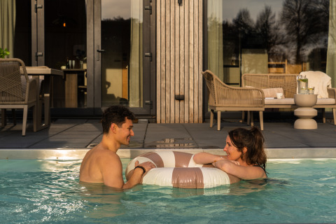 A young couple enjoying the heated pool at Unbrick One Lodge with sauna, modern outdoor seating in the background.