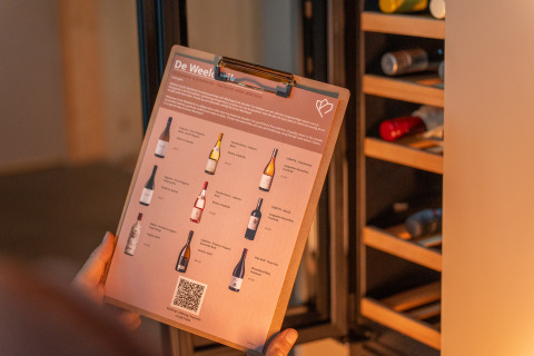 Una persona sostiene una carta de vinos frente a una vinoteca en Unbrick One Lodge con sauna y piscina.