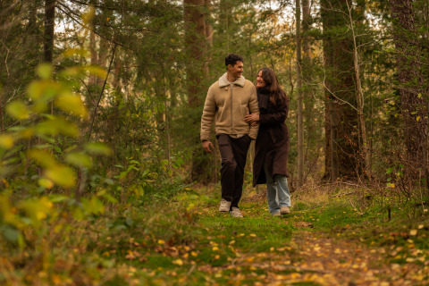 A couple walks together in a forest near Unbrick One | Sauna and Pool, surrounded by lush greenery.