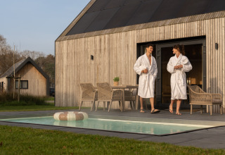 Pareja con albornoces disfruta de la terraza y la piscina en Unbrick One lodge en los Países Bajos.