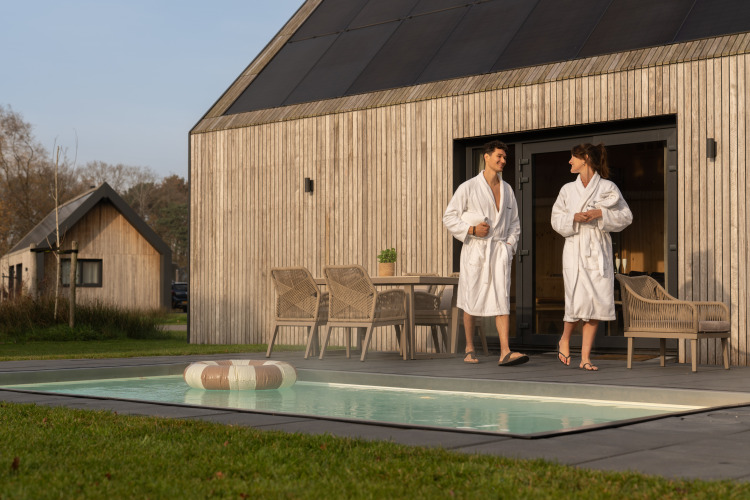 Pareja con albornoces disfruta de la terraza y la piscina en Unbrick One lodge en los Países Bajos.