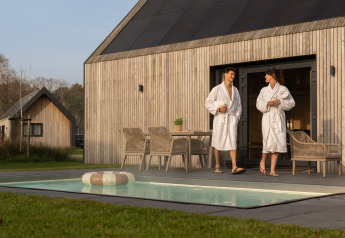 To personer i badekåber nyder terrassen og poolen ved en moderne træhytte på Unbrick One i Holland.