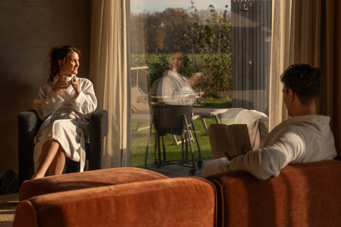 Dos personas se relajan con batas de baño en el interior de Unbrick One Lodge, De Weelderik, Países Bajos, al atardecer.