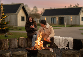 Two people relaxing by a campfire at Unbrick One | Sauna and Pool lodge at De Weelderik, Netherlands.