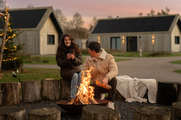 Zwei Personen entspannen am Lagerfeuer vor Cottages bei Unbrick One | Sauna and Pool in De Weelderik, Niederlande.