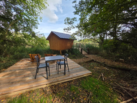 Glampinghut met houten terras, tafel en stoelen, gelegen midden in het groen en omgeven door natuur.