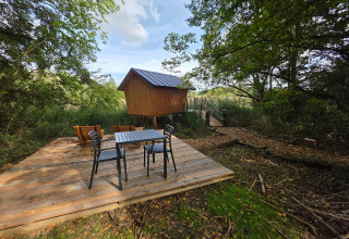 Glampinghut met houten terras, tafel en stoelen, gelegen midden in het groen en omgeven door natuur.
