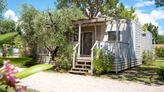 Photo of the Next XL Superiore lodge with a wooden deck, greenery, and a bright blue sky above.