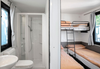 Kompakt badeværelse med bruser, toilet og vask ved siden af et værelse med køjesenge i Cottage Next.