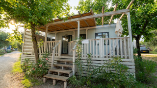 Exterior view of Cottage Next L 1/5 pers. lodge with a wooden porch, surrounded by trees and greenery.