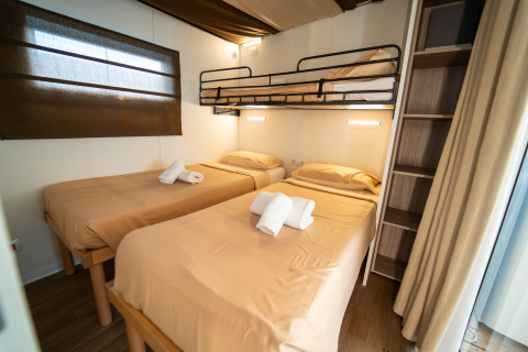 Interior de una habitación Cottage Clever en Vacanze Glamping Boutique Italia, con tres camas y estantería.