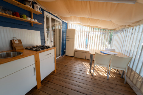 Cocina y comedor en Cottage Clever, Vacanze Glamping Boutique en Italia, con suelo de madera y toldo.