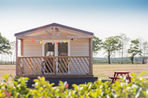 Beach Lodge con veranda in legno, festoni colorati e tavolo da picnic rosso in un paesaggio aperto.