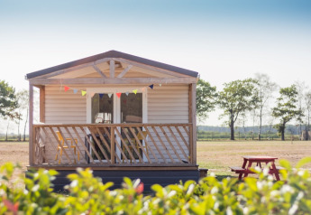 Beach Lodge con veranda in legno, festoni colorati e tavolo da picnic rosso in un paesaggio aperto.