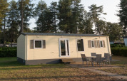 En Sun Lodge Comfort ved Arden Parks Tulderheyde i Belgien, omgivet af høje træer og udendørs siddemøbler.