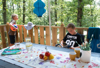 Deux garçons profitent de la terrasse d’une Lodge Tent Deluxe en Italie avec boissons, fruits et forêt.