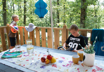 Due ragazzi si rilassano sulla terrazza di una Lodge Tent Deluxe in Italia con frutta, bevande e natura.