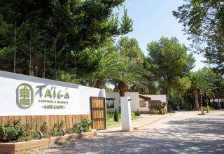 Entrance of TAIGA Lake Caspe holiday park in Aragón, Spain, surrounded by lush green trees and vibrant plants.