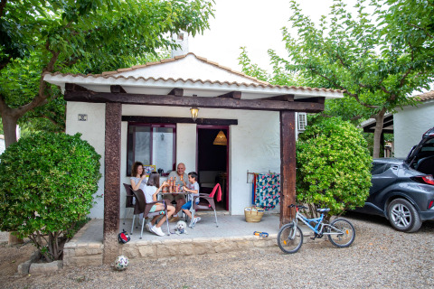 Gezin aan een tafeltje voor een chalet op TAIGA Lake Caspe vakantiepark in Aragón, Spanje.