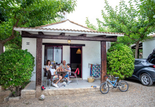 Family relaxes outside a cabin at TAIGA Lake Caspe holiday park in Aragón, Spain, with bike and dog.