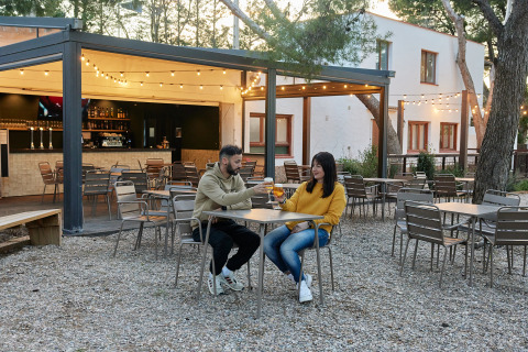Koppel proost op terras met lichtjes bij TAIGA Lake Caspe vakantiepark in Aragón, Spanje.